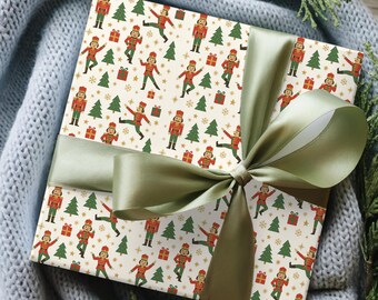 May include: A wrapped gift box with festive Christmas-themed wrapping paper. The paper features a repeating pattern of toy soldiers, Christmas trees, gift boxes, and snowflakes in red, green, and gold on a cream background. A sage green satin ribbon is tied around the box.