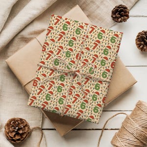 Pode incluir: Um presente embrulhado com papel de embrulho festivo com um padrão repetido dos números 6 e 7, gorros de Pai Natal e luzes de corda. O presente é amarrado com barbante e colocado sobre uma superfície neutra.