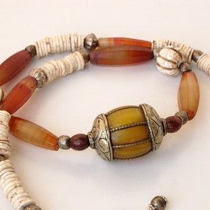 May include: A long necklace with brown, white, and yellow beads. The necklace has a large, yellow, barrel-shaped bead with silver accents.