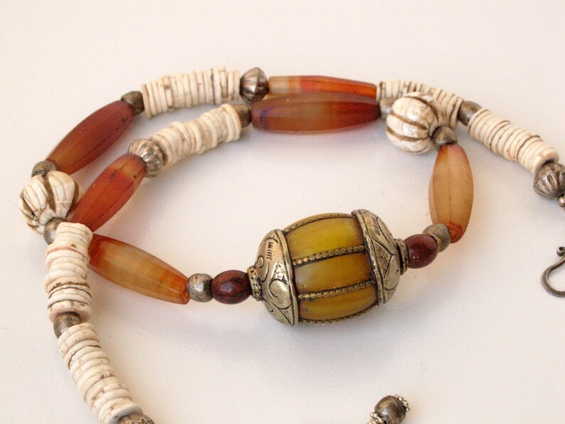 May include: A long necklace with brown, white, and yellow beads. The necklace has a large, yellow, barrel-shaped bead with silver accents.