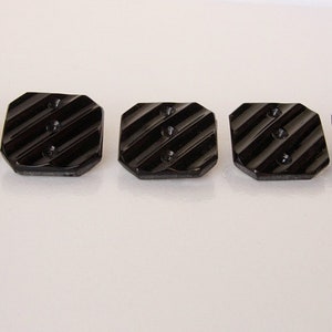 May include: Five black, octagonal buttons with a ridged surface and three holes each.