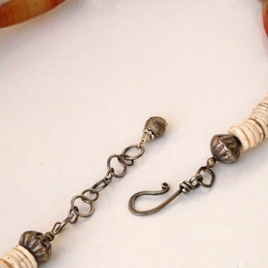 May include: A white and brown beaded necklace with a silver clasp and a silver bead at the end. The necklace is made of natural materials and has a rustic look.