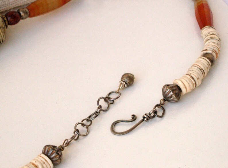 May include: A white and brown beaded necklace with a silver clasp and a silver bead at the end. The necklace is made of natural materials and has a rustic look.