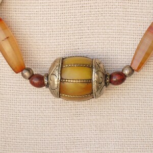 May include: A necklace made of orange, red, and white beads with a large yellow and gold bead in the center.