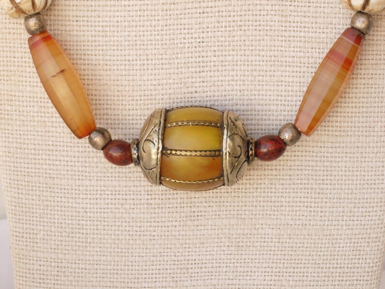 May include: A necklace made of orange, red, and white beads with a large yellow and gold bead in the center.