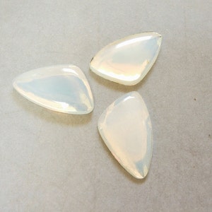 May include: Three iridescent white triangle-shaped glass stones. The stones are smooth and have a pearlescent finish.
