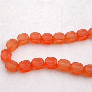 May include: A strand of orange glass beads, each bead is a square shape with rounded edges.