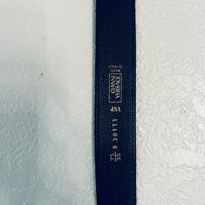 K&ouml;nnte beinhalten: Ein schwarzer Lederg&uuml;rtel mit dem Gianni Versace-Logo und dem Text "Made in Italy". Der G&uuml;rtel ist 76 cm lang und tr&auml;gt die Aufschrift "25 B 38111".