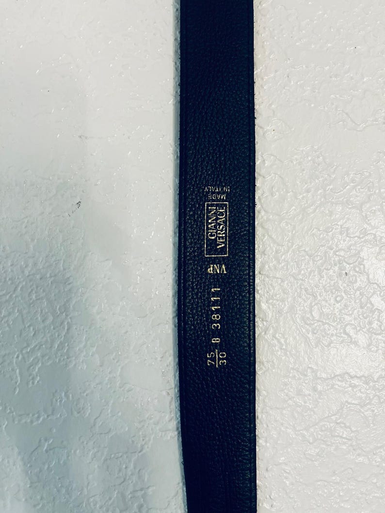 K&ouml;nnte beinhalten: Ein schwarzer Lederg&uuml;rtel mit dem Gianni Versace-Logo und dem Text "Made in Italy". Der G&uuml;rtel ist 76 cm lang und tr&auml;gt die Aufschrift "25 B 38111".