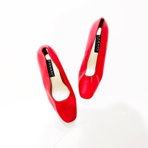 Puede incluir: Un par de zapatos de sal&oacute;n de cuero rojo con puntera cuadrada. Los zapatos tienen una etiqueta negra que dice "PARADE".