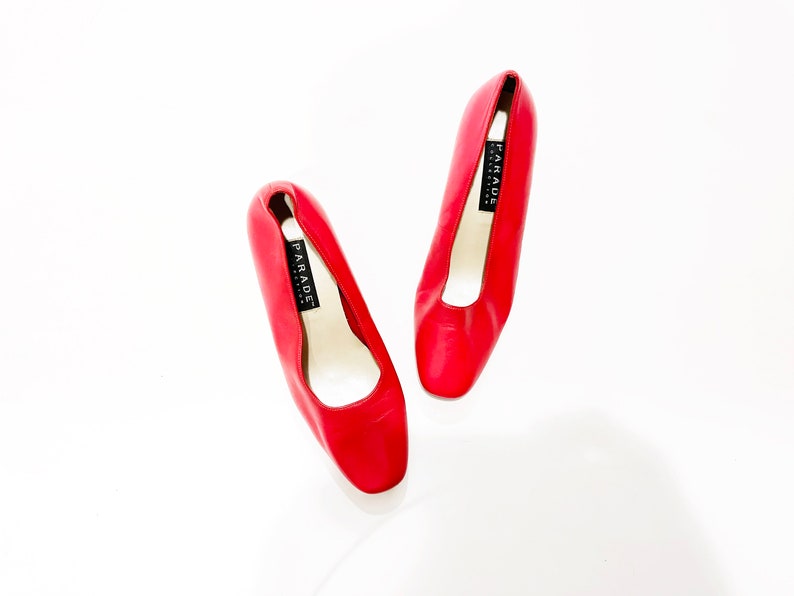 Puede incluir: Un par de zapatos de sal&oacute;n de cuero rojo con puntera cuadrada. Los zapatos tienen una etiqueta negra que dice "PARADE".