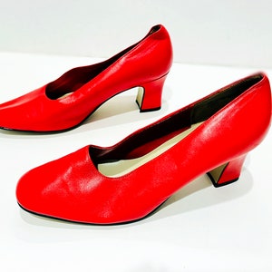 Puede incluir: Un par de zapatos de sal&oacute;n de cuero rojo con tac&oacute;n bajo de bloque. Los zapatos tienen punta puntiaguda y cierre trasero.