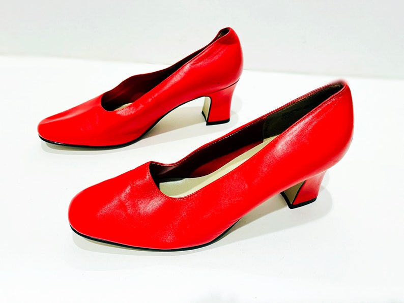 Puede incluir: Un par de zapatos de sal&oacute;n de cuero rojo con tac&oacute;n bajo de bloque. Los zapatos tienen punta puntiaguda y cierre trasero.
