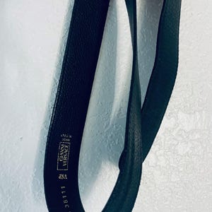 K&ouml;nnte beinhalten: Schwarzer Lederg&uuml;rtel mit dem Text "GIANNI VERSACE" und "MADE IN ITALY". Der G&uuml;rtel ist 75 cm lang. Der G&uuml;rtel ist dunkel und hat eine strukturierte Oberfl&auml;che.