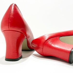 Puede incluir: Un par de zapatos de tac&oacute;n de cuero rojo con tac&oacute;n de bloque. Los zapatos est&aacute;n inclinados para mostrar la parte posterior de los tacones.