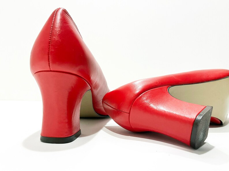 Puede incluir: Un par de zapatos de tac&oacute;n de cuero rojo con tac&oacute;n de bloque. Los zapatos est&aacute;n inclinados para mostrar la parte posterior de los tacones.