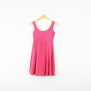 May include: A bright pink skater dress with a scoop neckline and a flared skirt. The dress is hanging on a wooden hanger against a white background. The sleeveless dress is made of a soft, textured fabric.