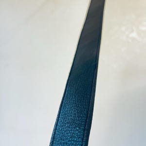 K&ouml;nnte beinhalten: Nahaufnahme eines dunkelblauen Lederriemens. Der Riemen hat eine strukturierte Oberfl&auml;che und ist an den Kanten vern&auml;ht. Der Riemen befindet sich vor einem wei&szlig;en Hintergrund.