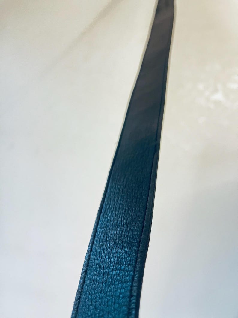 K&ouml;nnte beinhalten: Nahaufnahme eines dunkelblauen Lederriemens. Der Riemen hat eine strukturierte Oberfl&auml;che und ist an den Kanten vern&auml;ht. Der Riemen befindet sich vor einem wei&szlig;en Hintergrund.