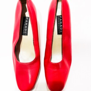 Puede incluir: Un par de zapatos de sal&oacute;n de cuero rojo con puntera cuadrada. Los zapatos tienen una etiqueta negra en el interior que dice "PARADE COLLECTION".