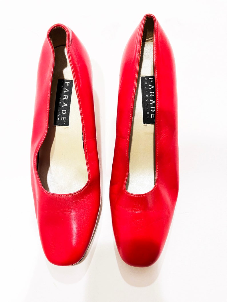 Puede incluir: Un par de zapatos de sal&oacute;n de cuero rojo con puntera cuadrada. Los zapatos tienen una etiqueta negra en el interior que dice "PARADE COLLECTION".