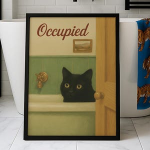 May include: Framed art print showing a black cat in a bathtub, with the word "Occupied". A blue towel with tiger illustrations hangs nearby. The bathroom has white tiles. The print is in a black frame.