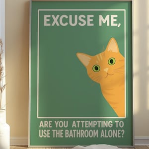 May include: A framed poster with a green background and the text "EXCUSE ME, ARE YOU ATTEMPTING TO USE THE BATHROOM ALONE?" features an orange cat peeking from the side. The cat has green eyes and a smiling expression.