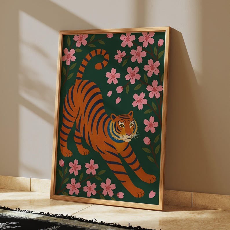 May include: A framed art print featuring an orange tiger with blue stripes stretching across a dark green background. Pink cherry blossoms and green leaves surround the tiger. The artwork is in a wooden frame.