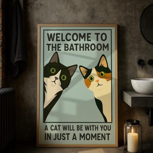 May include: Framed poster with a light blue background featuring two cartoon cats peeking from the sides. The text reads "WELCOME TO THE BATHROOM" and "A CAT WILL BE WITH YOU IN JUST A MOMENT". The frame is a light brown color.