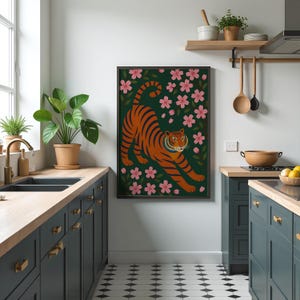 May include: A framed art print featuring an orange tiger with black stripes, set against a dark green background with pink cherry blossoms. The tiger is in a stretching pose. The artwork is displayed in a modern kitchen setting.