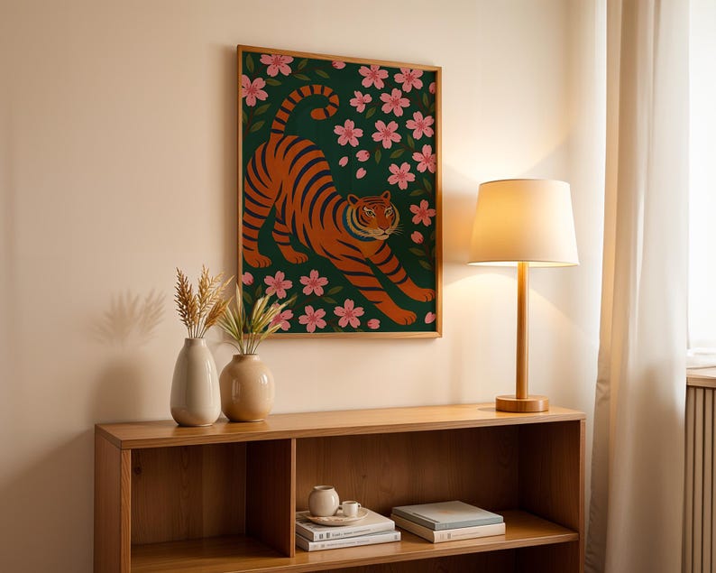 May include: A framed art print featuring an orange tiger with black stripes, set against a dark green background with pink cherry blossoms. The artwork is displayed above a wooden shelf with decorative vases and a lamp.