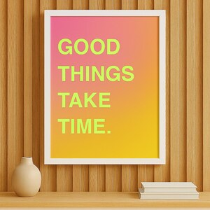 Könnte beinhalten: Ein gerahmter Druck mit dem Text "GOOD THINGS TAKE TIME" in leuchtend grünen Buchstaben vor einem Hintergrund mit Farbverlauf aus Rosa, Orange und Gelb. Eine kleine beige Vase und zwei Bücher stehen auf einem Holzregal.