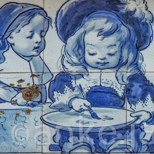 May include: A blue and white tile painting depicting three children. The child in the center is painting on a white plate. The child on the left is wearing a blue and white dress and the child on the right is wearing a blue and white dress with a white apron.