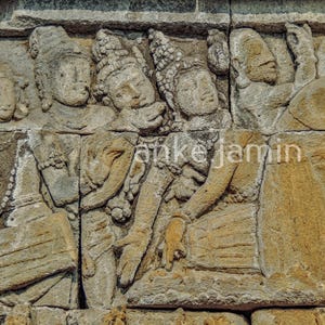 Può includere: Un'intagliatura a rilievo in pietra dettagliata raffigurante figure con copricapi e abiti ornati. L'opera d'arte, nei toni del beige e del grigio, mostra più figure che interagiscono, con dettagli visibili di mani e lineamenti del viso. Il nome dell'artista, "anke jamin", è visibile.