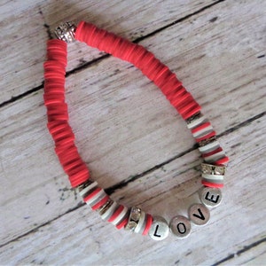 May include: Red and silver beaded bracelet with the word "LOVE" spelled out in silver letter beads. The bracelet features red disc beads and silver accent beads, with a silver clasp.