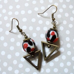 May include: A pair of earrings with a geometric triangle design and a black, white, and red patterned glass bead.