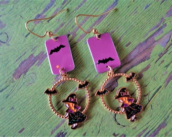 May include: Halloween-themed earrings with gold-colored hooks. Each earring features a purple rectangular top with a black bat and a star. Below, a gold-colored ring with a witch and bats.