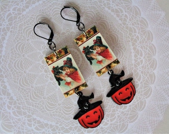 May include: A pair of Halloween-themed earrings. Each earring features a rectangular charm with a vintage illustration of a girl in a red cape and a witch hat, holding a black cat. Below, a smiling orange pumpkin with a black witch hat.