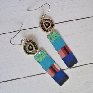 Pode incluir: Brincos pendurados com detalhes em metal prateado. Os pingentes retangulares apresentam um design de patchwork em tons de azul, turquesa, vermelho e preto. Fechamento por gancho. Os brincos têm cerca de 5 cm de comprimento.