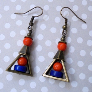 May include: A pair of geometric earrings with bronze-colored metal triangles. Each earring features an orange bead, a blue bead, and a bronze-colored metal triangle. The earrings have bronze-colored ear wires.