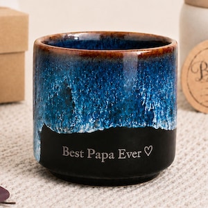 May include: A ceramic mug with a blue and black glaze, featuring the text "Best Papa Ever" in white. The mug has a brown rim and is likely a Father's Day gift.
