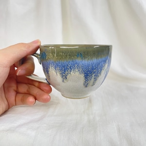 May include: A ceramic mug with a blue, green, and white glaze. The mug has a rounded shape and a handle.