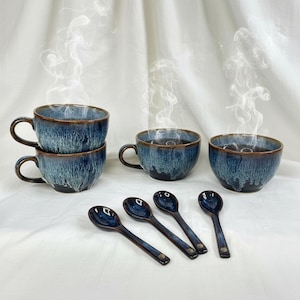 May include: A set of six ceramic teacups and spoons. The cups and spoons are a deep blue with brown trim. Steam rises from the cups, suggesting they contain a hot beverage. The spoons are arranged in front of the cups on a white surface.