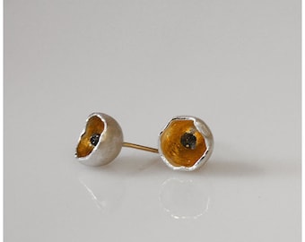 Puede incluir: Un par de pendientes de plata con interior dorado y centro negro. Los pendientes tienen forma de flor.