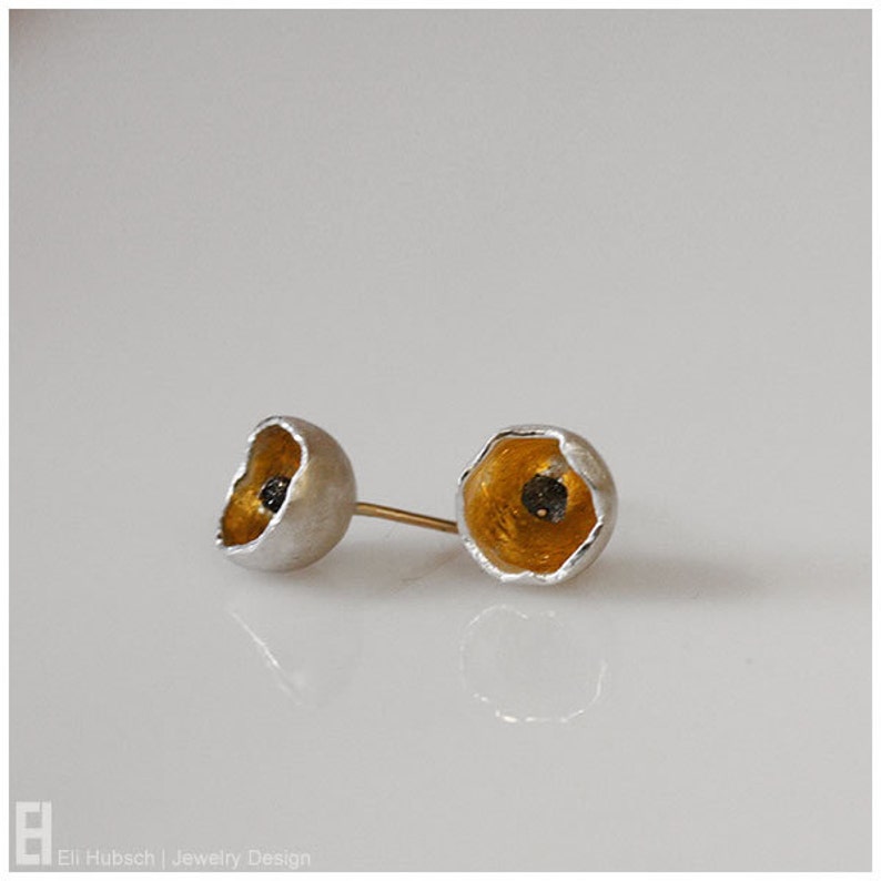 May include: A pair of silver earrings with a gold interior and a black center. The earrings are shaped like a flower.