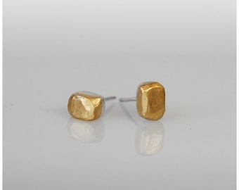 Op de afbeelding: Een paar gouden en zilveren oorbel studs met een gehamerde textuur. De oorbellen zijn klein en vierkant.