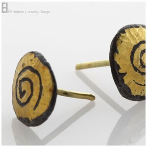 Peut inclure: Une paire de boucles d'oreilles dorées et noires avec un motif en spirale. Les boucles d'oreilles sont en métal et ont un fermoir à tige.