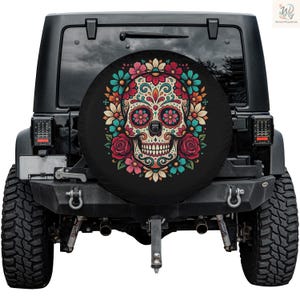 May include: Black spare tire cover featuring a colorful sugar skull design. The skull is decorated with floral patterns in shades of pink, blue, and orange, surrounded by a wreath of flowers. The cover is mounted on a black Jeep.