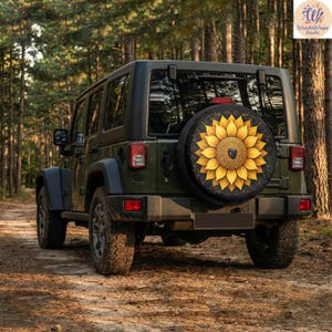 Könnte beinhalten: Ein dunkelgrüner Jeep mit einer schwarzen Reserveradabdeckung mit einem großen gelben Sonnenblumenmuster. Die Sonnenblume hat komplizierte Details und ein dunkles Zentrum. Der Jeep steht auf einer unbefestigten Straße, umgeben von Bäumen.
