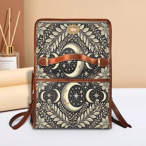 Peut inclure: Sac à dos rectangulaire avec un motif céleste représentant des croissants de lune, des étoiles et des motifs floraux en noir, crème et marron. Le sac a des sangles, une poignée et des bordures en cuir marron. Fermeture à rabat avec fermoir doré.
